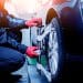 Volante puxando para um lado? 2 Car mechanic installing sensor during suspension adjustment. Wheel alignment work at repair service station