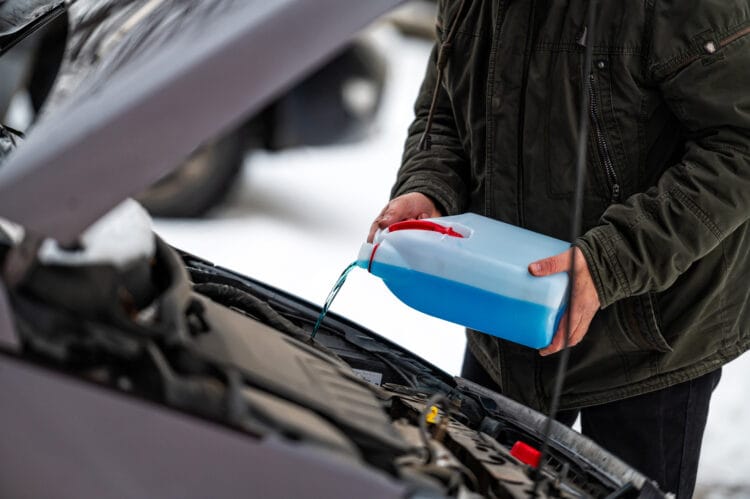 driver refilling the blue non-freezing windshield washer liquid in the tank of the car, closeup