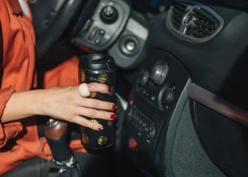 Motorista segurando um copo térmico no interior do carro, representando conforto, segurança e acessórios automotivos que facilitam o dia a dia ao dirigir.
