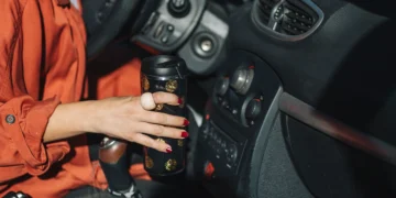 Motorista segurando um copo térmico no interior do carro, representando conforto, segurança e acessórios automotivos que facilitam o dia a dia ao dirigir.
