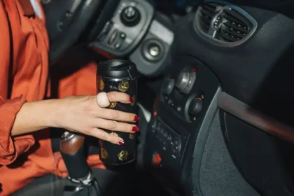 Motorista segurando um copo t&eacute;rmico no interior do carro, representando conforto, seguran&ccedil;a e acess&oacute;rios automotivos que facilitam o dia a dia ao dirigir.