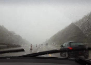 Vista de estrada sob forte tempestade, com chuva intensa e baixa visibilidade através do para-brisa do carro, simbolizando o alerta laranja do Inmet com ventos acima de 90 km/h e riscos no trânsito.