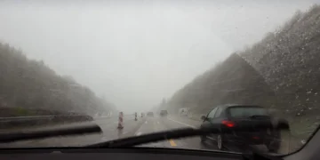 Vista de estrada sob forte tempestade, com chuva intensa e baixa visibilidade através do para-brisa do carro, simbolizando o alerta laranja do Inmet com ventos acima de 90 km/h e riscos no trânsito.