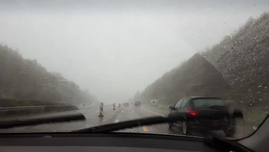 Vista de estrada sob forte tempestade, com chuva intensa e baixa visibilidade através do para-brisa do carro, simbolizando o alerta laranja do Inmet com ventos acima de 90 km/h e riscos no trânsito.