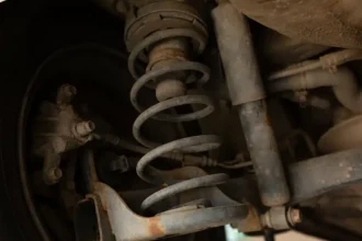 Suspensão de veículo mostrando amortecedor gasto com sinais de ferrugem e vazamento de óleo, destacando a importância da manutenção para segurança e estabilidade.