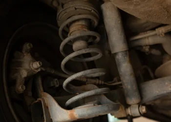 Suspensão de veículo mostrando amortecedor gasto com sinais de ferrugem e vazamento de óleo, destacando a importância da manutenção para segurança e estabilidade.