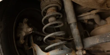 Suspensão de veículo mostrando amortecedor gasto com sinais de ferrugem e vazamento de óleo, destacando a importância da manutenção para segurança e estabilidade.