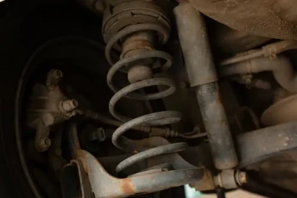 Suspens&atilde;o de ve&iacute;culo mostrando amortecedor gasto com sinais de ferrugem e vazamento de &oacute;leo, destacando a import&acirc;ncia da manuten&ccedil;&atilde;o para seguran&ccedil;a e estabilidade.