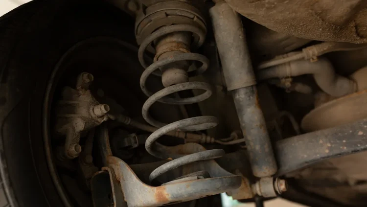 Suspensão de veículo mostrando amortecedor gasto com sinais de ferrugem e vazamento de óleo, destacando a importância da manutenção para segurança e estabilidade.