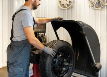 Mecânico realizando o balanceamento de rodas em uma máquina de oficina, ajustando o peso do pneu para garantir estabilidade e reduzir vibrações no veículo.