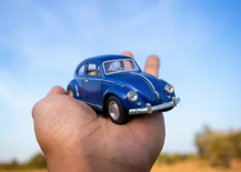 Carro vira miniatura digital: guia 2025 para transformar seu automóvel em viral nas redes sociais 1 Mão segurando um Fusca azul em miniatura sob um céu azul, representando a tendência de transformar carros reais em versões digitais com aparência de miniatura para posts criativos e virais nas redes sociais.