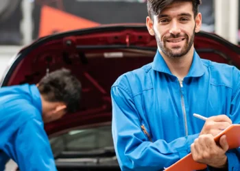 Mecânico sorridente em oficina realizando checklist de revisão de veículo antes de uma viagem, simbolizando a importância da manutenção preventiva e da preparação do carro para trajetos longos com segurança e tranquilidade.