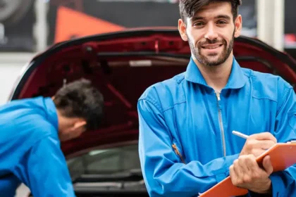 Mec&acirc;nico sorridente em oficina realizando checklist de revis&atilde;o de ve&iacute;culo antes de uma viagem, simbolizando a import&acirc;ncia da manuten&ccedil;&atilde;o preventiva e da prepara&ccedil;&atilde;o do carro para trajetos longos com seguran&ccedil;a e tranquilidade.