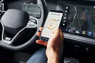 Motorista segura um smartphone com aplicativo de economia de energia enquanto o painel do carro exibe informações de navegação, ilustrando a integração entre conectividade automotiva, infotainment e telemetria nos veículos de 2025.
