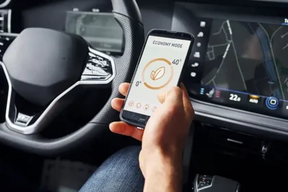 Motorista segura um smartphone com aplicativo de economia de energia enquanto o painel do carro exibe informa&ccedil;&otilde;es de navega&ccedil;&atilde;o, ilustrando a integra&ccedil;&atilde;o entre conectividade automotiva, infotainment e telemetria nos ve&iacute;culos de 2025.