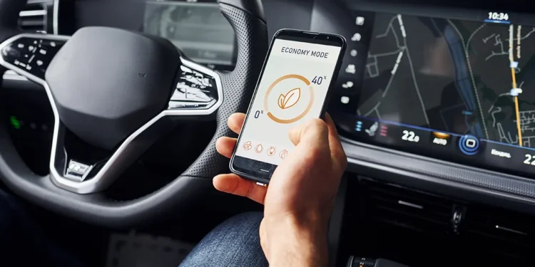 Motorista segura um smartphone com aplicativo de economia de energia enquanto o painel do carro exibe informações de navegação, ilustrando a integração entre conectividade automotiva, infotainment e telemetria nos veículos de 2025.