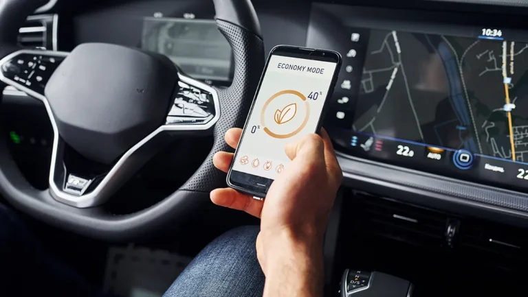 Motorista segura um smartphone com aplicativo de economia de energia enquanto o painel do carro exibe informações de navegação, ilustrando a integração entre conectividade automotiva, infotainment e telemetria nos veículos de 2025.
