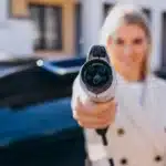 Mulher segurando um plugue de carregamento de carro elétrico em destaque, simbolizando a transição tecnológica dos veículos flex-híbridos que combinam etanol, gasolina e energia elétrica.