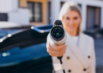 Mulher segurando um plugue de carregamento de carro elétrico em destaque, simbolizando a transição tecnológica dos veículos flex-híbridos que combinam etanol, gasolina e energia elétrica.