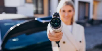 Mulher segurando um plugue de carregamento de carro elétrico em destaque, simbolizando a transição tecnológica dos veículos flex-híbridos que combinam etanol, gasolina e energia elétrica.