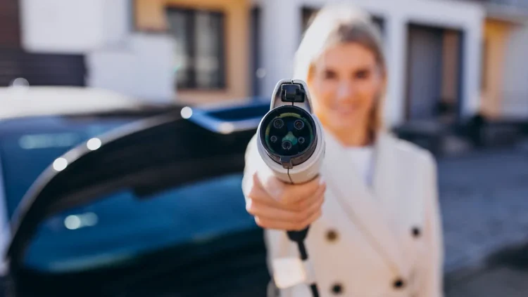 Mulher segurando um plugue de carregamento de carro elétrico em destaque, simbolizando a transição tecnológica dos veículos flex-híbridos que combinam etanol, gasolina e energia elétrica.