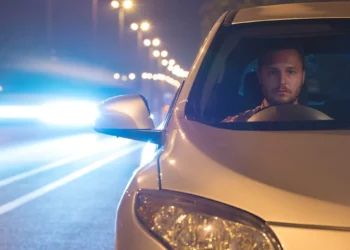 Motorista dirige à noite em rodovia iluminada, com o farol do carro ligado e outro veículo vindo em sentido oposto, representando a aplicação da Lei do Farol Automotivo e a importância da iluminação correta para segurança nas estradas.