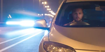 Motorista dirige à noite em rodovia iluminada, com o farol do carro ligado e outro veículo vindo em sentido oposto, representando a aplicação da Lei do Farol Automotivo e a importância da iluminação correta para segurança nas estradas.