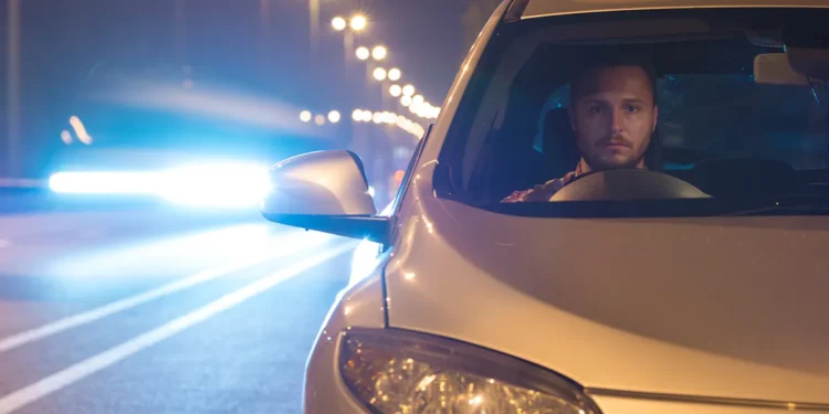 Motorista dirige à noite em rodovia iluminada, com o farol do carro ligado e outro veículo vindo em sentido oposto, representando a aplicação da Lei do Farol Automotivo e a importância da iluminação correta para segurança nas estradas.