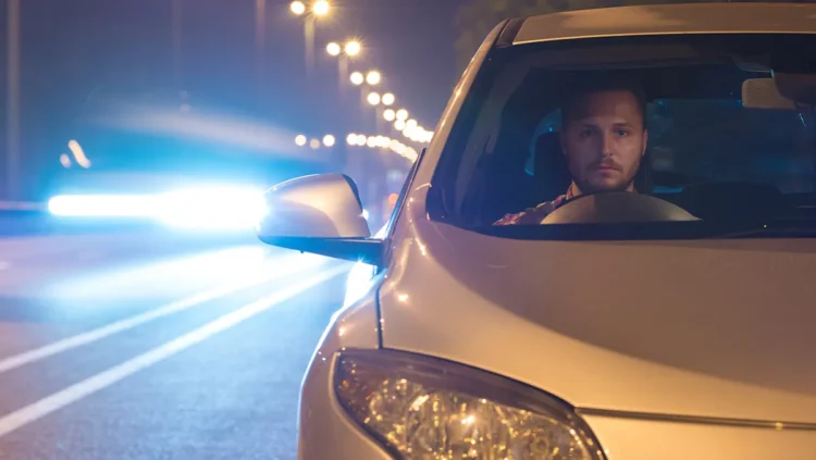 Motorista dirige à noite em rodovia iluminada, com o farol do carro ligado e outro veículo vindo em sentido oposto, representando a aplicação da Lei do Farol Automotivo e a importância da iluminação correta para segurança nas estradas.