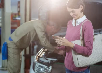 Mecânico atendendo cliente em oficina moderna, com mulher segurando celular ao lado do carro, representando a nova era da manutenção preventiva automotiva com foco em veículos elétricos, híbridos e conectados.