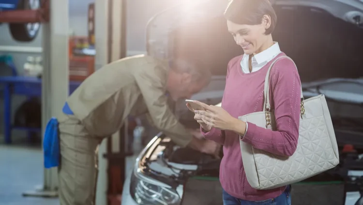 Mecânico atendendo cliente em oficina moderna, com mulher segurando celular ao lado do carro, representando a nova era da manutenção preventiva automotiva com foco em veículos elétricos, híbridos e conectados.