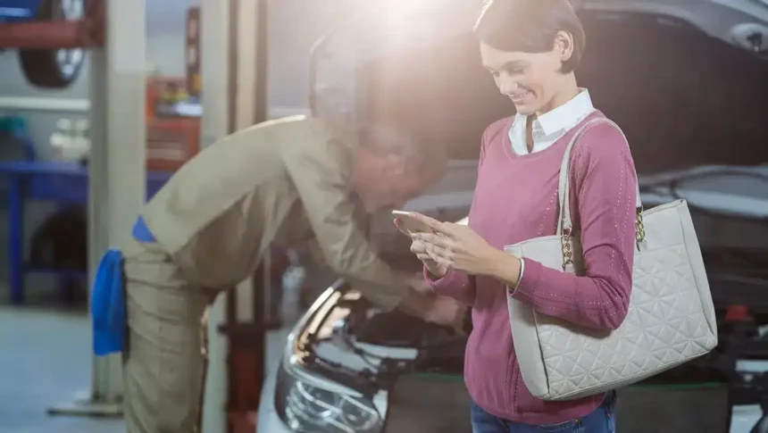 Mecânico atendendo cliente em oficina moderna, com mulher segurando celular ao lado do carro, representando a nova era da manutenção preventiva automotiva com foco em veículos elétricos, híbridos e conectados.