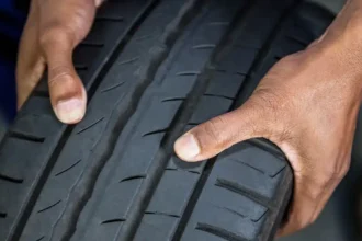 Pessoa verificando o desenho da banda de rodagem de um pneu de inverno, destacando os sulcos profundos e o padrão próprio para maior aderência em pistas molhadas ou frias.