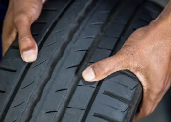 Pessoa verificando o desenho da banda de rodagem de um pneu de inverno, destacando os sulcos profundos e o padrão próprio para maior aderência em pistas molhadas ou frias.