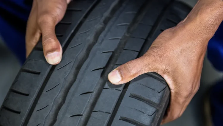 Pessoa verificando o desenho da banda de rodagem de um pneu de inverno, destacando os sulcos profundos e o padrão próprio para maior aderência em pistas molhadas ou frias.