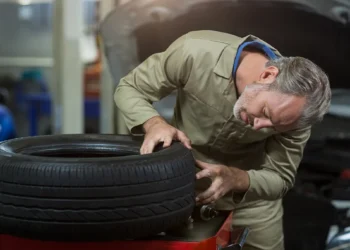 Mecânico inspecionando um pneu remold em oficina automotiva, verificando a qualidade da banda de rodagem e o estado da borracha reformada.