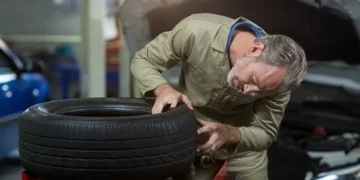 Mecânico inspecionando um pneu remold em oficina automotiva, verificando a qualidade da banda de rodagem e o estado da borracha reformada.