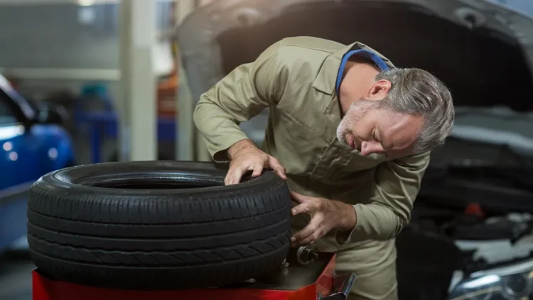Mecânico inspecionando um pneu remold em oficina automotiva, verificando a qualidade da banda de rodagem e o estado da borracha reformada.