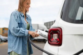 Mulher conectando cabo de recarga em carro elétrico branco em estação pública, representando o crescimento das vendas de veículos elétricos no Brasil e a expansão da infraestrutura de recarga.