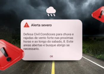 Painel de alerta climático em estrada sob chuva intensa, com vento forte e pista molhada, representando o aviso do Inmet sobre risco de ciclone extratropical e interdições nas rodovias BR-101 e BR-116.