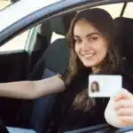 Mulher sorridente dentro de um carro segurando sua CNH, simbolizando a conquista da habilitação gratuita pelo programa CNH Social destinado a pessoas de baixa renda.
