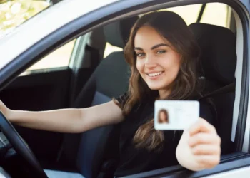 Mulher sorridente dentro de um carro segurando sua CNH, simbolizando a conquista da habilitação gratuita pelo programa CNH Social destinado a pessoas de baixa renda.