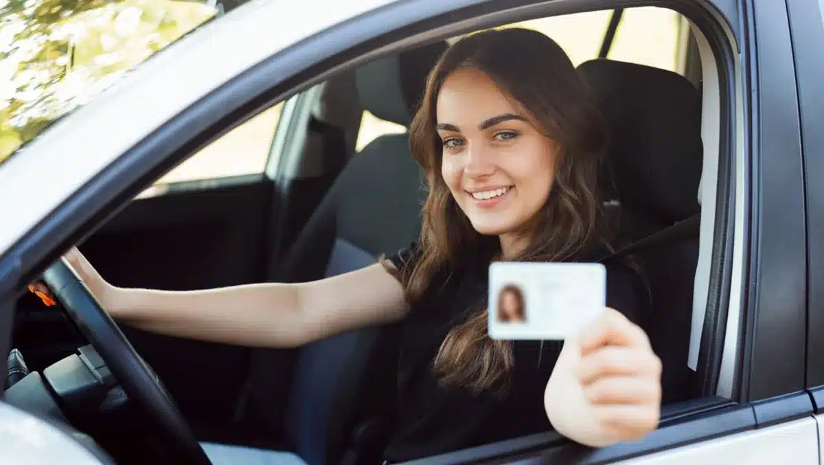 Mulher sorridente dentro de um carro segurando sua CNH, simbolizando a conquista da habilitação gratuita pelo programa CNH Social destinado a pessoas de baixa renda.