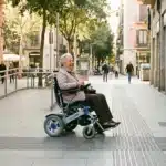 Pessoa idosa usando cadeira de rodas elétrica pagará IPVA em 2026 numa rua urbana acessível