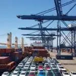Cena de porto de Santos com navios carregados de carros elétricos da BYD sob céu ensolarado, destacando importação de carros elétricos que