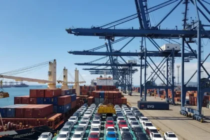 Cena de porto de Santos com navios carregados de carros el&eacute;tricos da BYD sob c&eacute;u ensolarado, destacando importa&ccedil;&atilde;o de carros el&eacute;tricos que