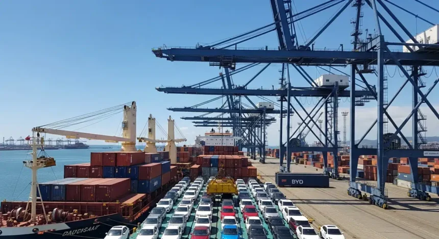 Cena de porto de Santos com navios carregados de carros elétricos da BYD sob céu ensolarado, destacando importação de carros elétricos que