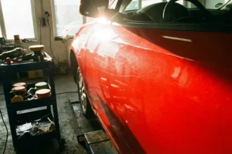 Carro com foco na porta, destacando riscos leves e microrelevo sob o sol, ferramentas de polimento ao lado na oficina