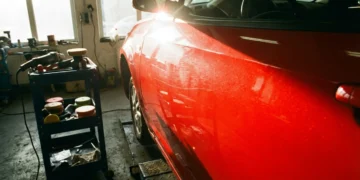 Carro com foco na porta, destacando riscos leves e microrelevo sob o sol, ferramentas de polimento ao lado na oficina