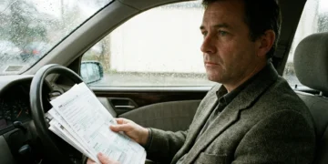 Motorista pensativo segurando contas de impostos dentro do carro, refletindo sobre 13 salário e prioridades como IPVA e licenciamento